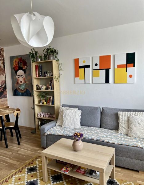 Living room in a two-room apartment with a sofa, table, and wooden decor flooring.