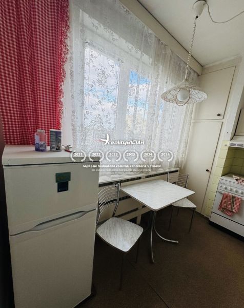A kitchen in a 3-room apartment, with a refrigerator and a table, curtains, red checkered drapes.