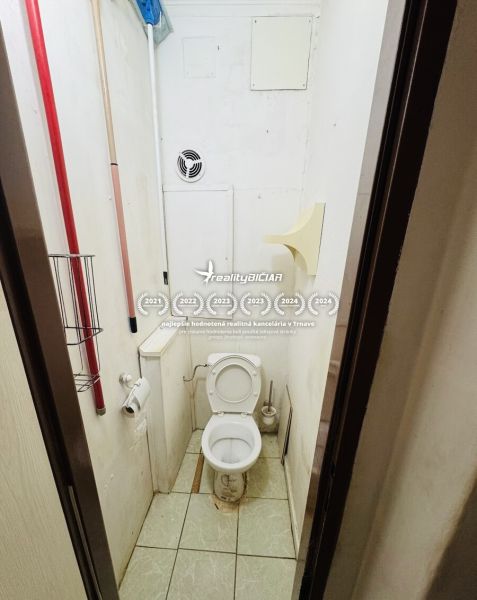 The interior with ceramic tiles includes a toilet with a ventilation opening and cleaning supplies.