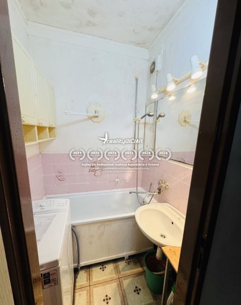 Bathroom with a bathtub, washing machine, and sink in a 3-room apartment, pink tiles, ceiling lighting.