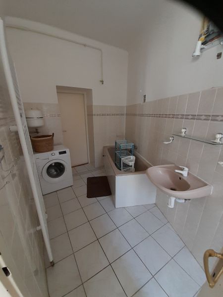 A bathroom in a 4-room apartment with a washing machine, bathtub, and sink on white tiles.