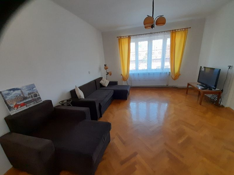 Living room with wood-patterned flooring, sofa, television, and yellow curtains.