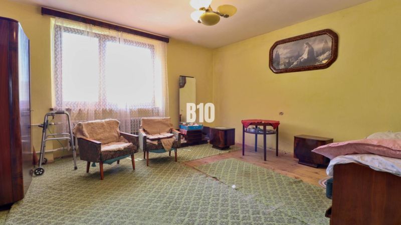 A room in a family house with armchairs, a table, and carpeted flooring.