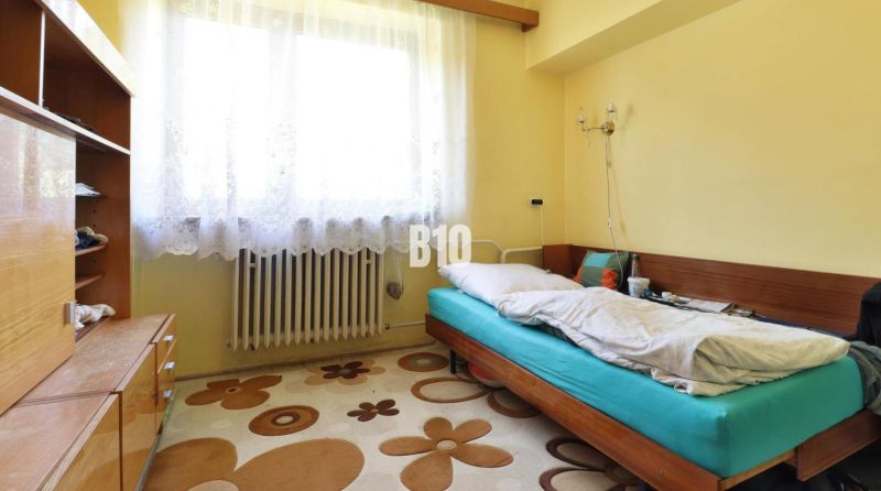 A room in a family house with a single bed, a wardrobe, and a window with white curtains.