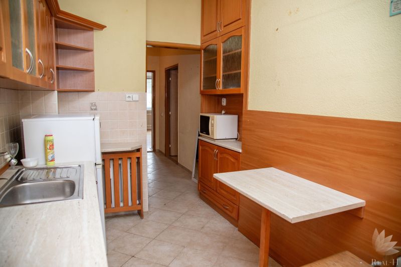 A kitchen with wooden cabinets, a sink, a microwave, and a dining counter in a two-room apartment.