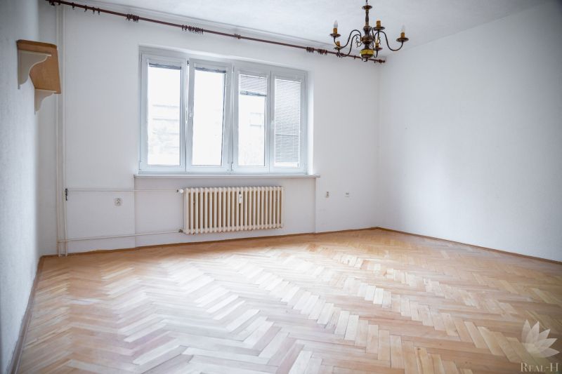 Empty room with a chandelier, white walls, and a wooden-patterned floor.