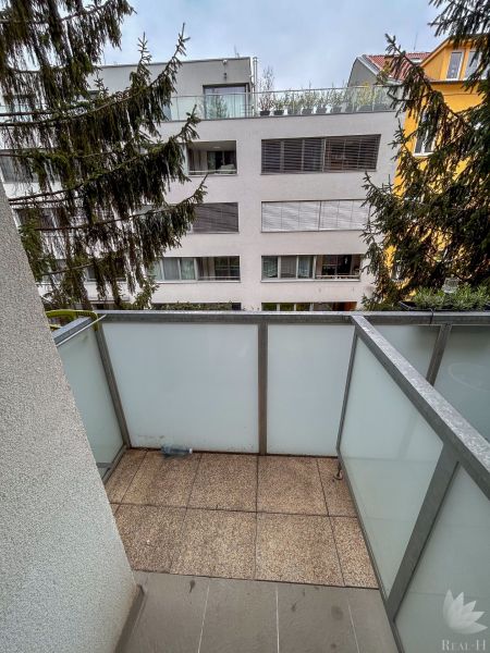 A balcony of a 2-room apartment with a view of neighboring apartment buildings and a tree in Bratislava.