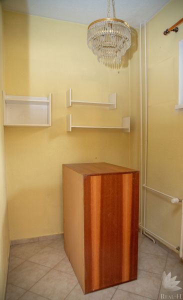 A room in a 2-room apartment with a chandelier, shelves, and tiles.