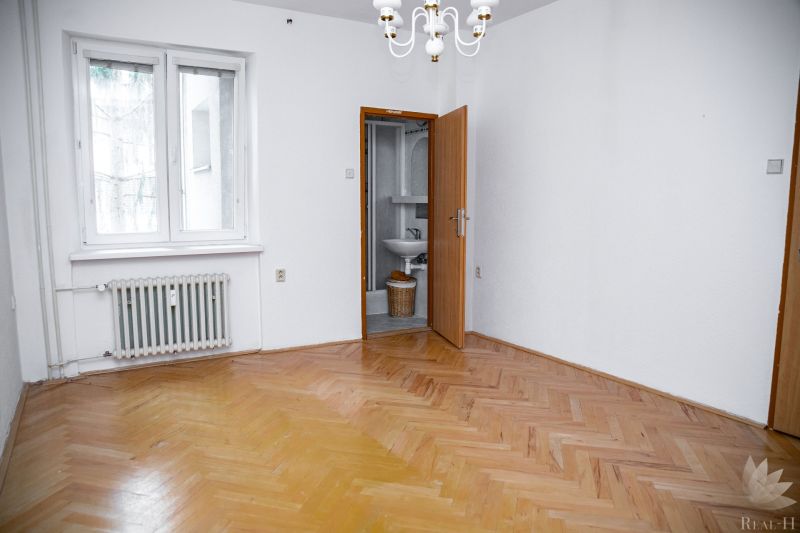 A room with a wooden floor decor, white walls, and a radiator in a 2-room apartment.