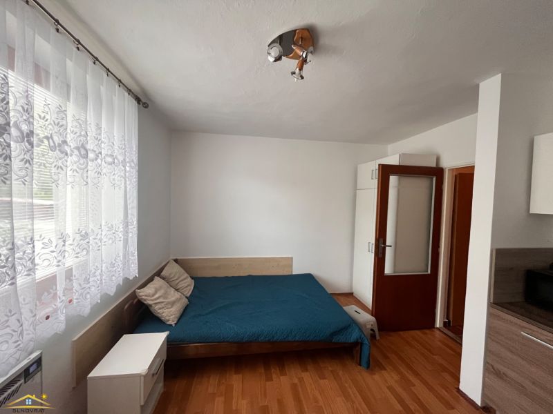 Studio apartment with curtains, bed, and wooden decor flooring.