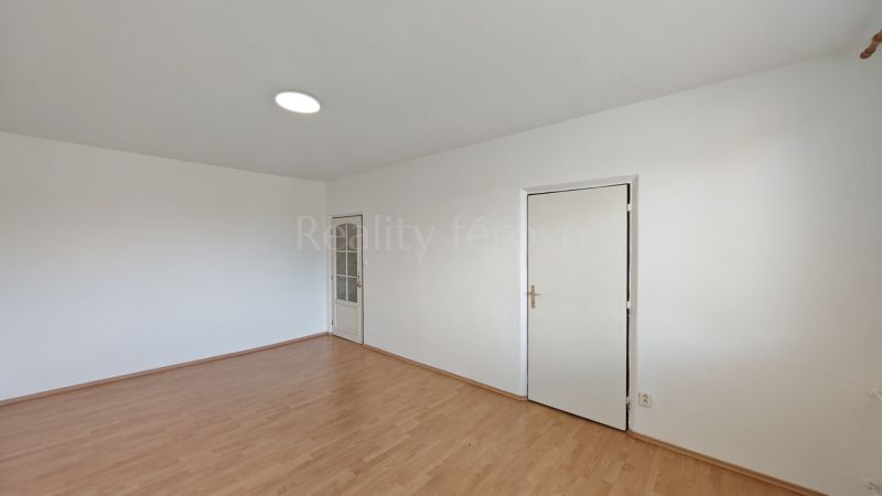 A room in a 2-room apartment with a wooden decor floor and white walls.