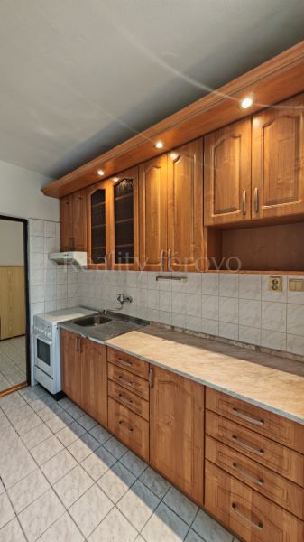 A kitchen in a 2-room apartment with a wooden decor kitchen unit and white tiles.
