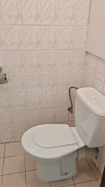 A bathroom in a 2-room apartment with a toilet, white tiles, and light flooring.