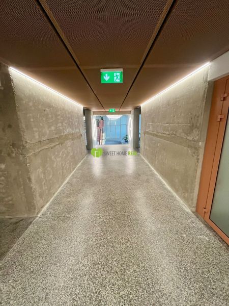 A hallway with concrete walls and a terrazzo floor in a 2-room apartment.