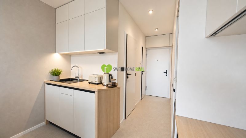 A kitchen in a 2-room apartment with white cabinets and a wooden decor.