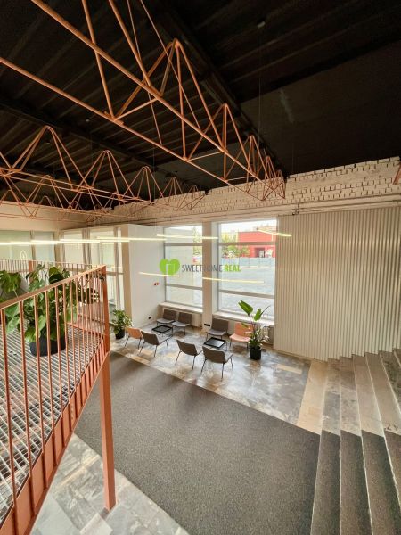 A large interior with metal ceiling structures, a staircase, and seating in a studio apartment.