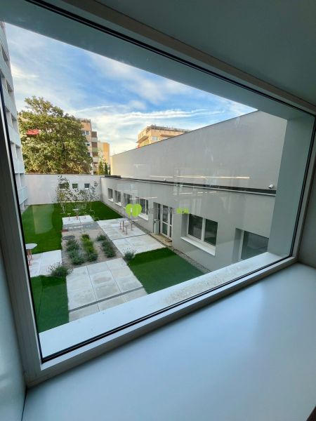 A view from the window of a one-room apartment onto an inner courtyard with greenery and benches.