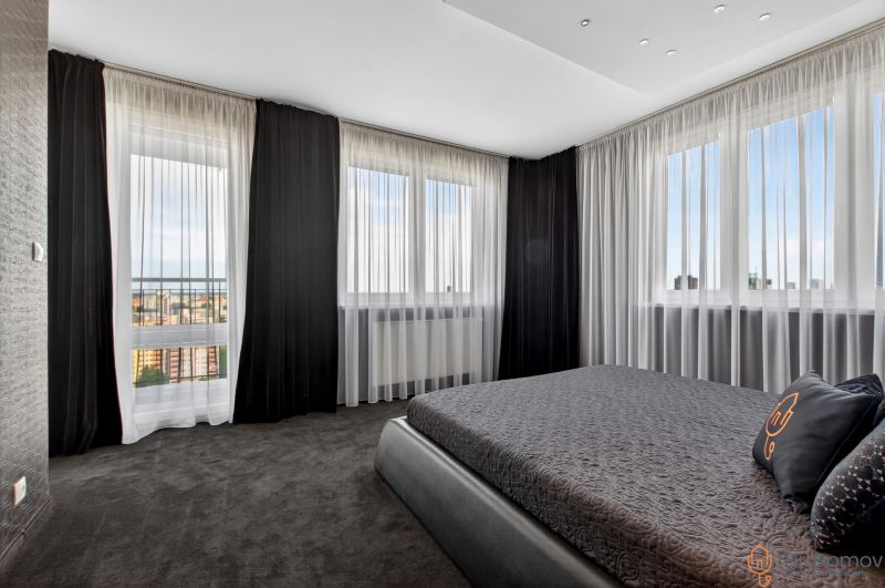 A bedroom in a 4-room apartment with dark curtains and a view of the city.
