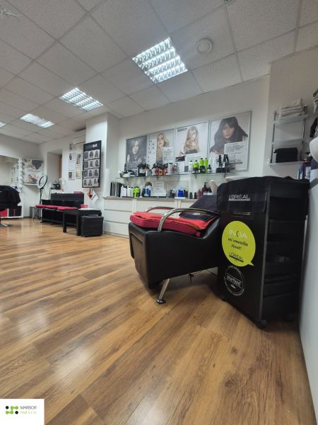 Commercial space with wood-patterned flooring, hairdressing chairs, and products on the wall.