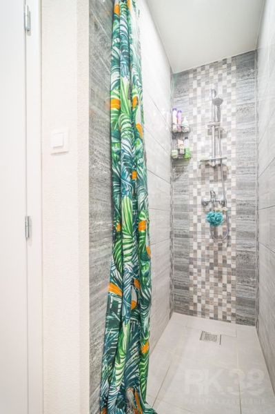 A shower corner with tiles and a colorful curtain in a 2-room apartment.