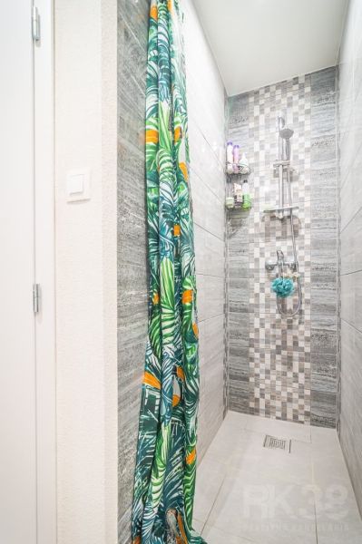 A shower corner in a 2-room apartment with a colorful curtain and wall tiles.