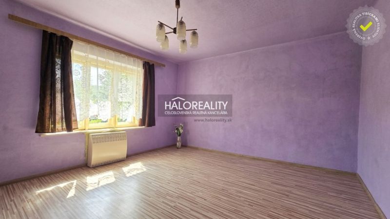 A room with purple walls, a light fixture, a wooden-patterned floor, and a window with dark curtains.