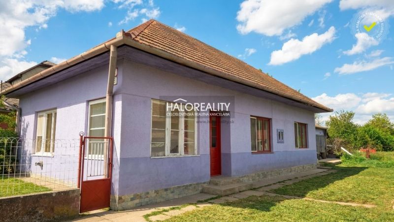A family house in Lok with a purple facade, red doors, and a sloped roof.