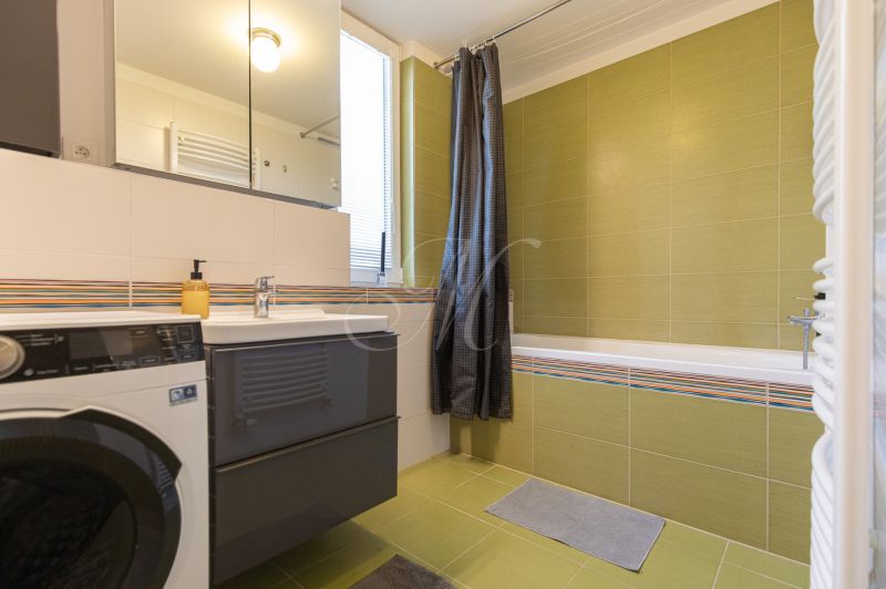 A bathroom in a 2-room apartment with a bathtub, washing machine, and mirrored cabinet.