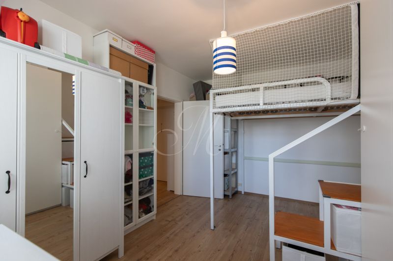 A room with a bunk bed, cabinets, and a wooden decor floor in a two-room apartment.