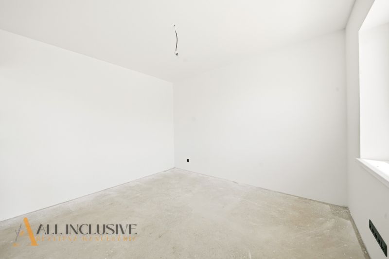An empty room in a family house with white walls and an unfinished floor.