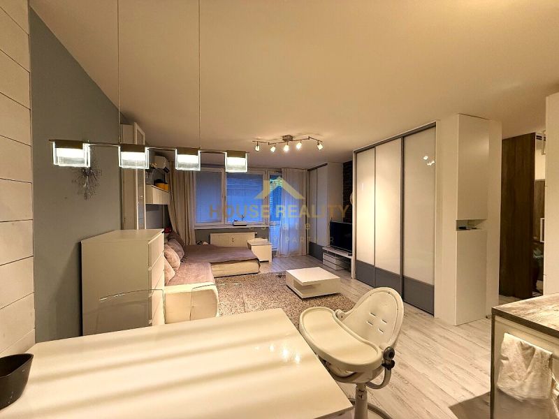 Interior of a 2-room apartment with a wooden decor floor, a large sofa, and a dining table.