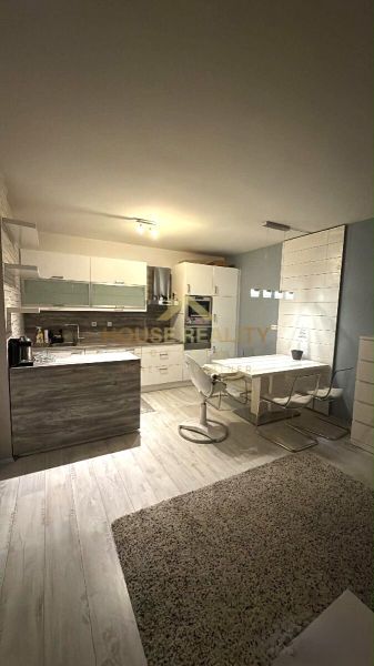 A kitchen area in a two-room apartment with a wood-patterned floor, a dining table, and a kitchen unit.
