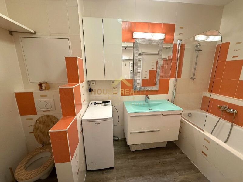 Bathroom in a 2-room apartment with a bathtub, washing machine, and orange tiles.