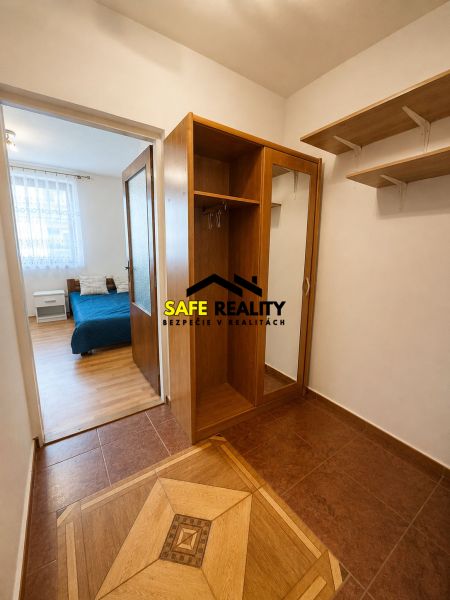 Studio apartment with wood-patterned flooring, built-in wardrobe, and a bed in the background.
