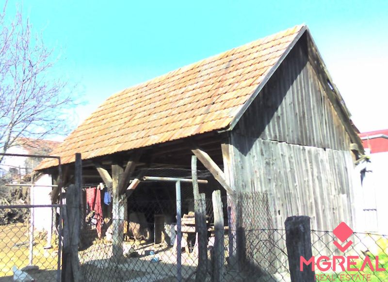 A wooden shed next to a family house in Nové Sady with a red tile roof.