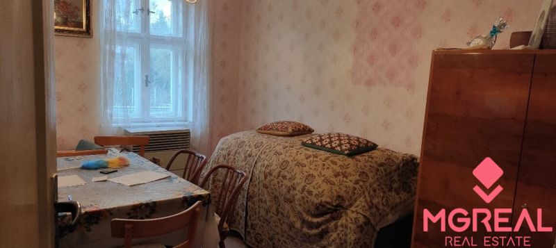 A room in a family house with floral wallpaper, a table, and a bed by the window.