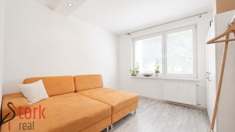 A room in a 3-room apartment with an orange sofa and a wooden decor floor.