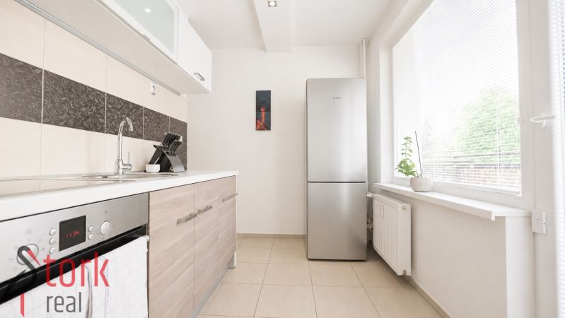 A kitchen in a 3-room apartment with tiles and a refrigerator, bright lighting.
