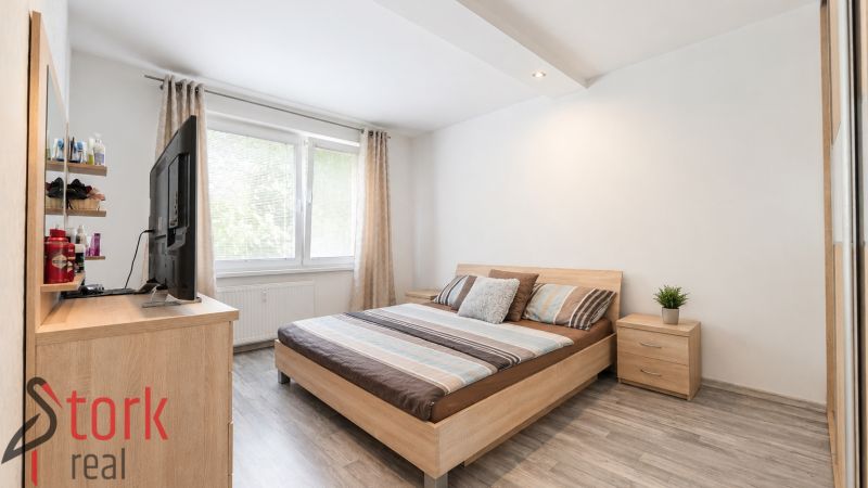 A bright bedroom with a bed and a wooden decor floor in a 3-room apartment.
