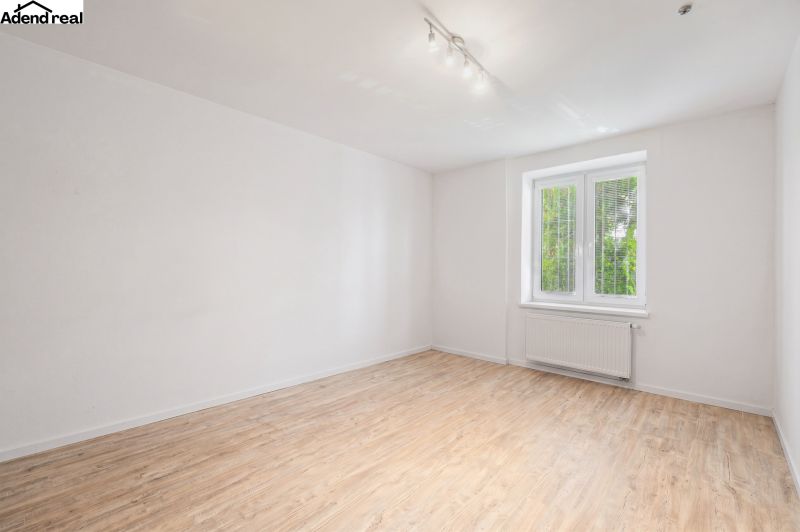 White room in a family house with a wood-patterned floor and a window.