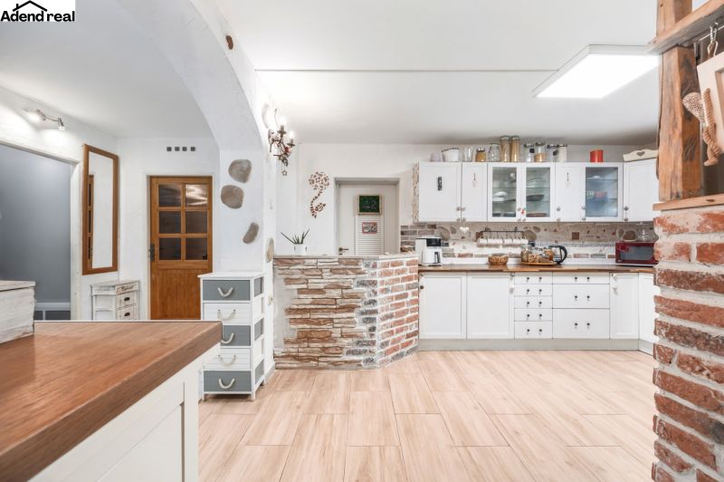 A kitchen in a family house with white cabinets, brick elements, and a wooden-patterned floor.