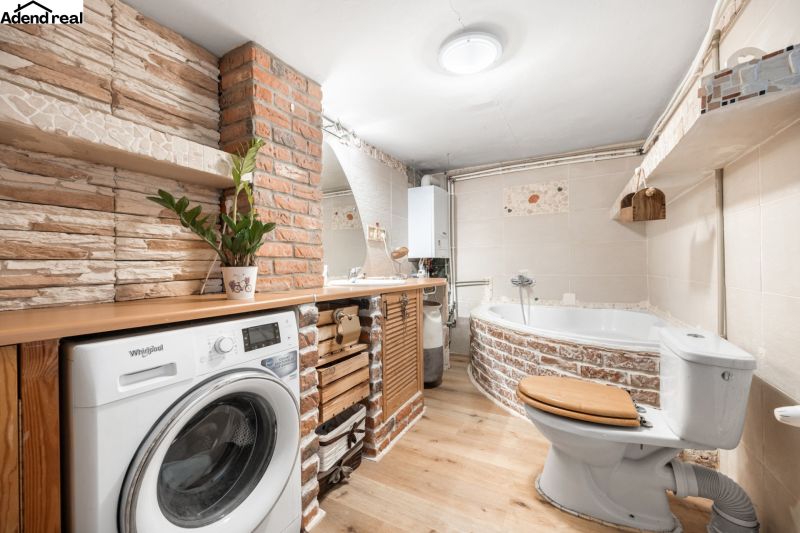 A bathroom in a family house with a bathtub, a washing machine, and a wooden decor floor.