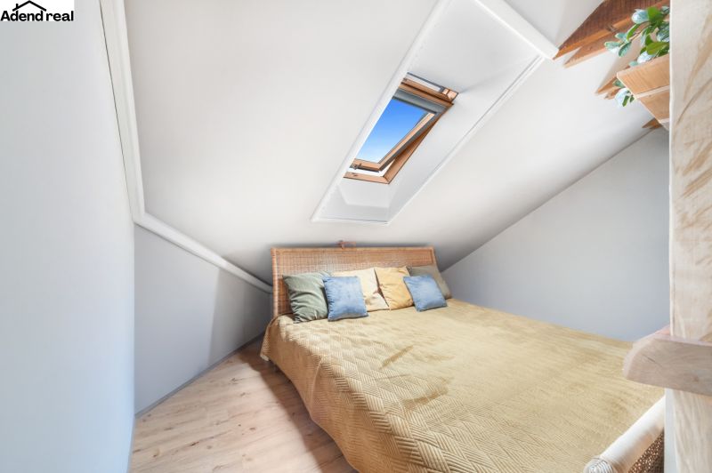 Attic room in a family house with a bed, skylight, and wooden decor flooring.