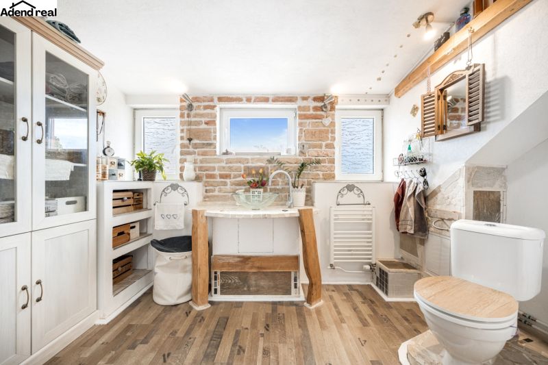 A bathroom in a family house with a brick wall, a wooden decor floor, and rustic decorations.