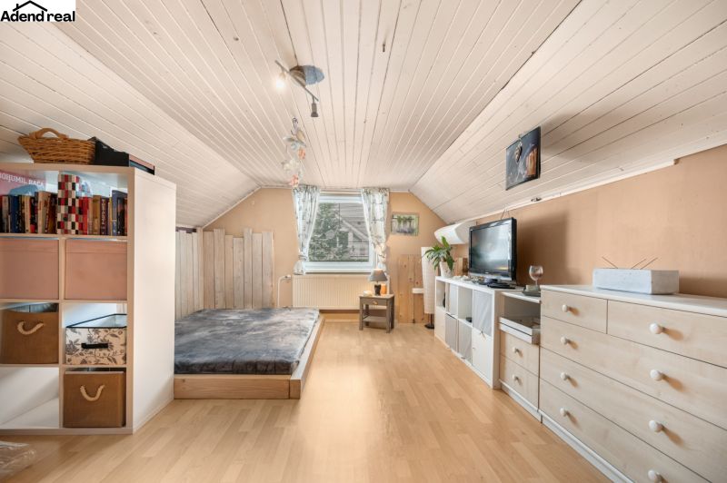 Attic room of a family house with a bed, dresser, and shelves, floor with wooden decor.