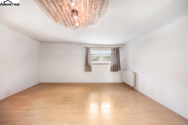 A room in a family house with a wooden decor floor, a radiator, and a small window.