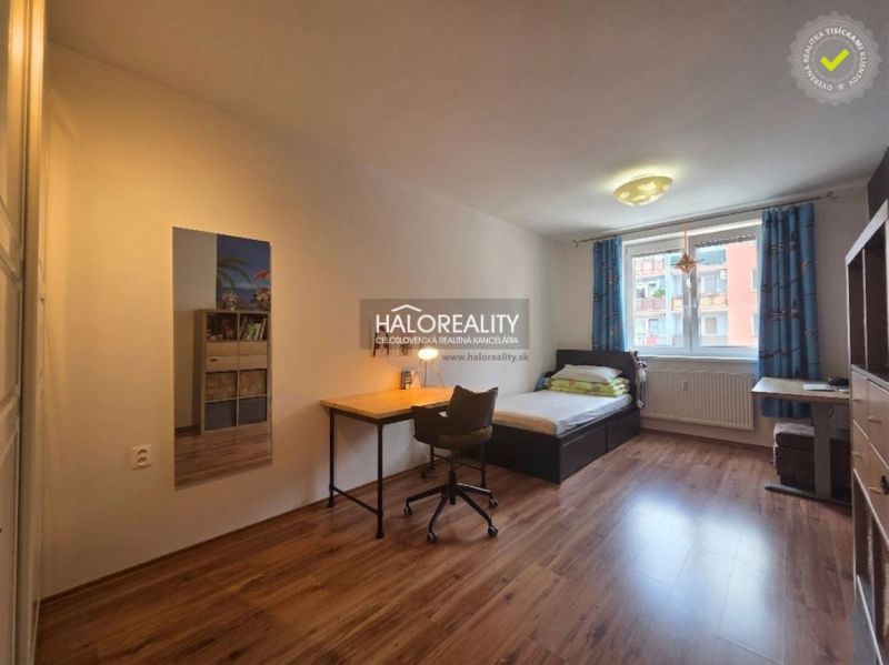 A room in a 2-room apartment with a desk and a wooden decor floor.