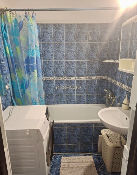 A bathroom with a bathtub, washing machine, blue tiles, and a shower curtain in a 3-room apartment.