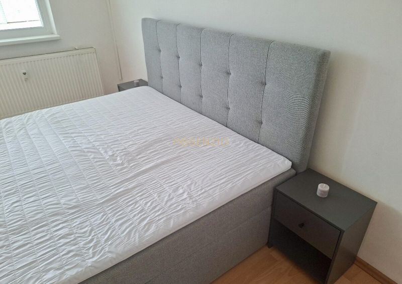Gray bed with upholstered headboard and nightstand in a 3-room apartment.