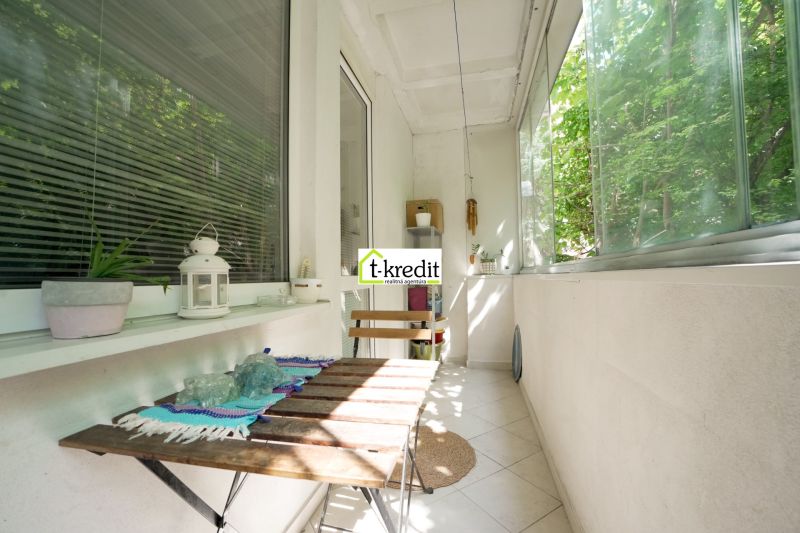Balcony in a 3-room apartment with a wooden table and greenery in the background.